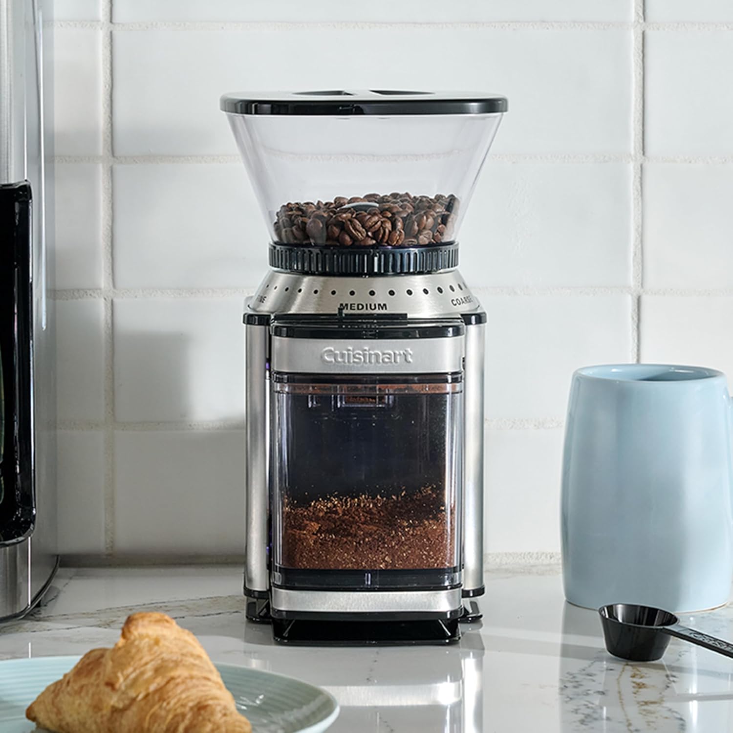 Stainless steel burr coffee grinder full of beans on a white kitchen counter